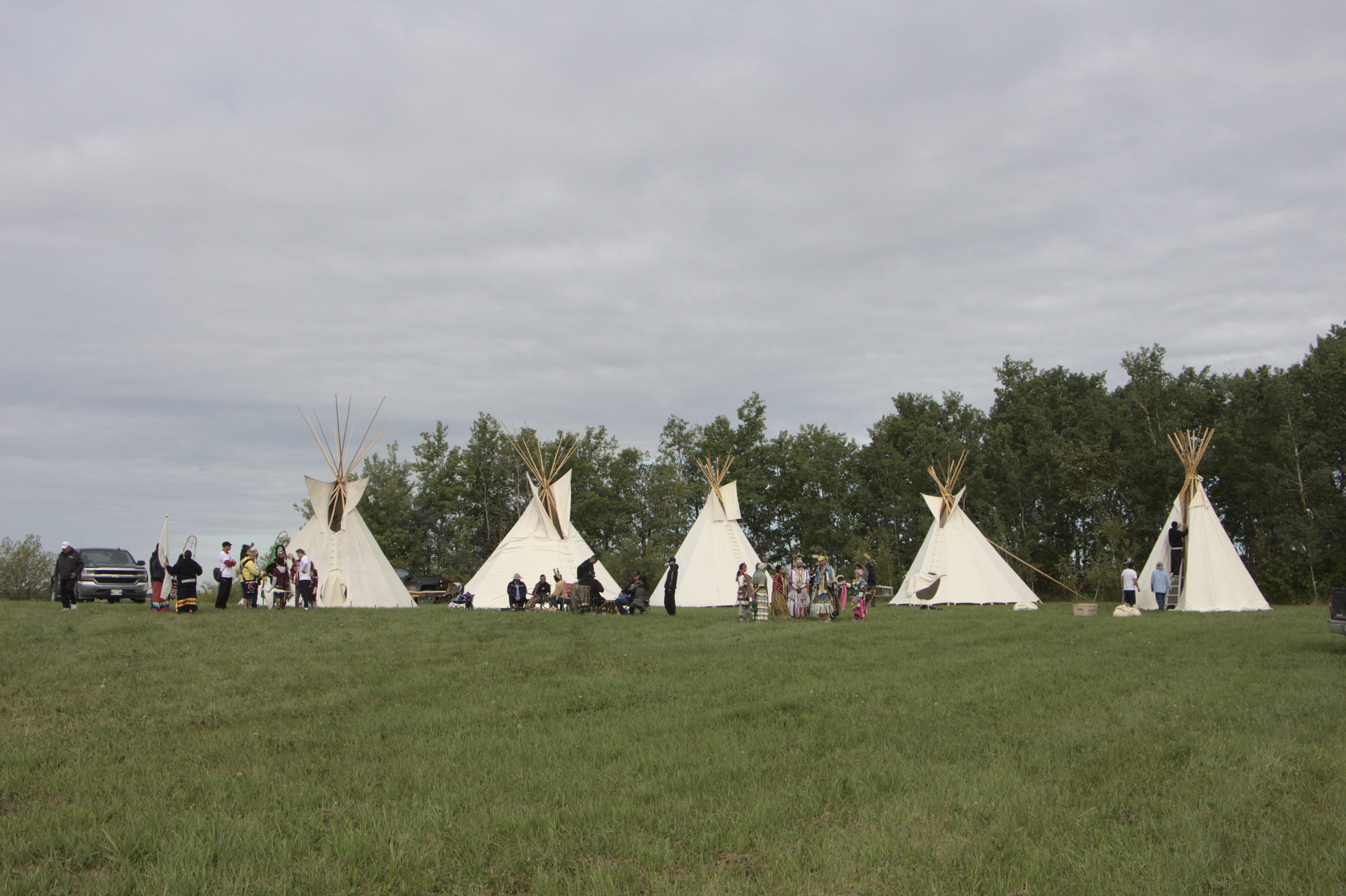 Five teepees set up and people dressed for ceremony